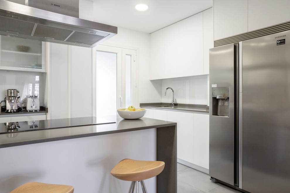 Offene Moderne Küche in U-Form mit weißen Schränken, Küchengeräten aus Edelstahl, Kücheninsel, grauem Boden und grauer Arbeitsplatte in Madrid