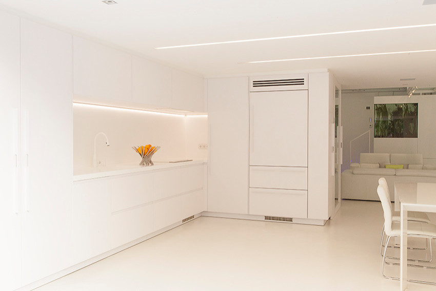 バルセロナにある広いコンテンポラリースタイルのおしゃれなキッチン (一体型シンク、落し込みパネル扉のキャビネット、白いキャビネット、白いキッチンパネル、白い調理設備、コンクリートの床、アイランドなし、白い床、白いキッチンカウンター) の写真