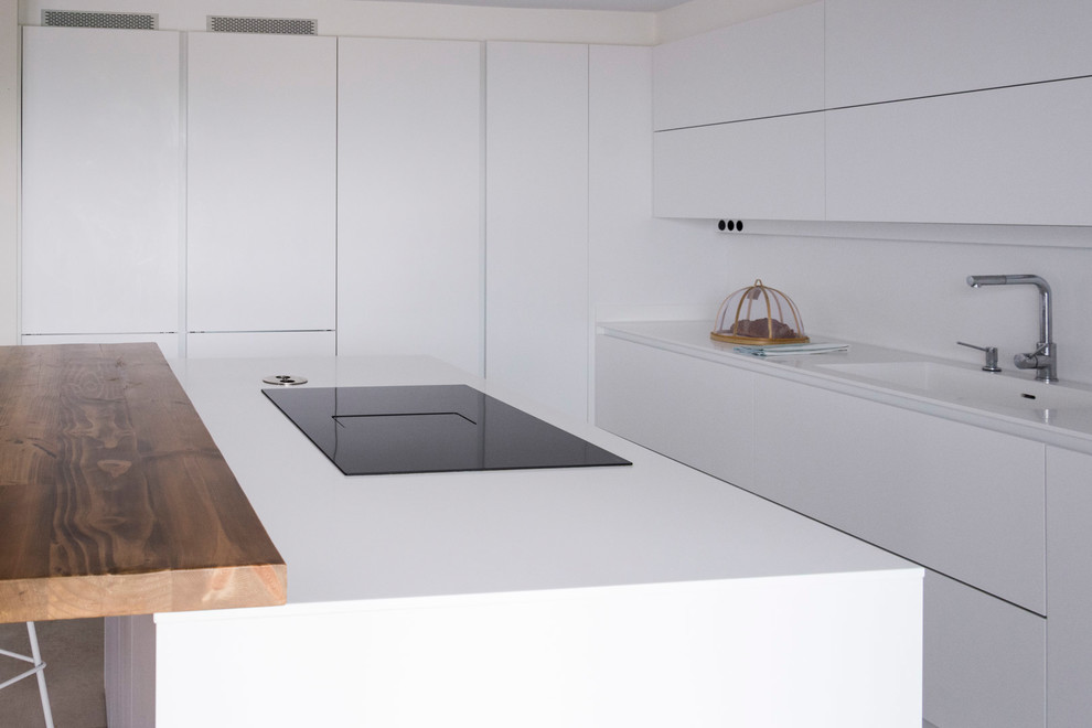 Imagen de cocina minimalista abierta con fregadero integrado, armarios con paneles lisos, puertas de armario blancas, salpicadero blanco, una isla y encimeras blancas
