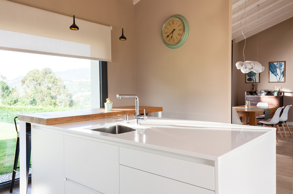 Foto di una cucina design con lavello sottopiano, ante lisce, ante bianche, top in quarzo composito, paraspruzzi bianco, elettrodomestici neri e pavimento marrone