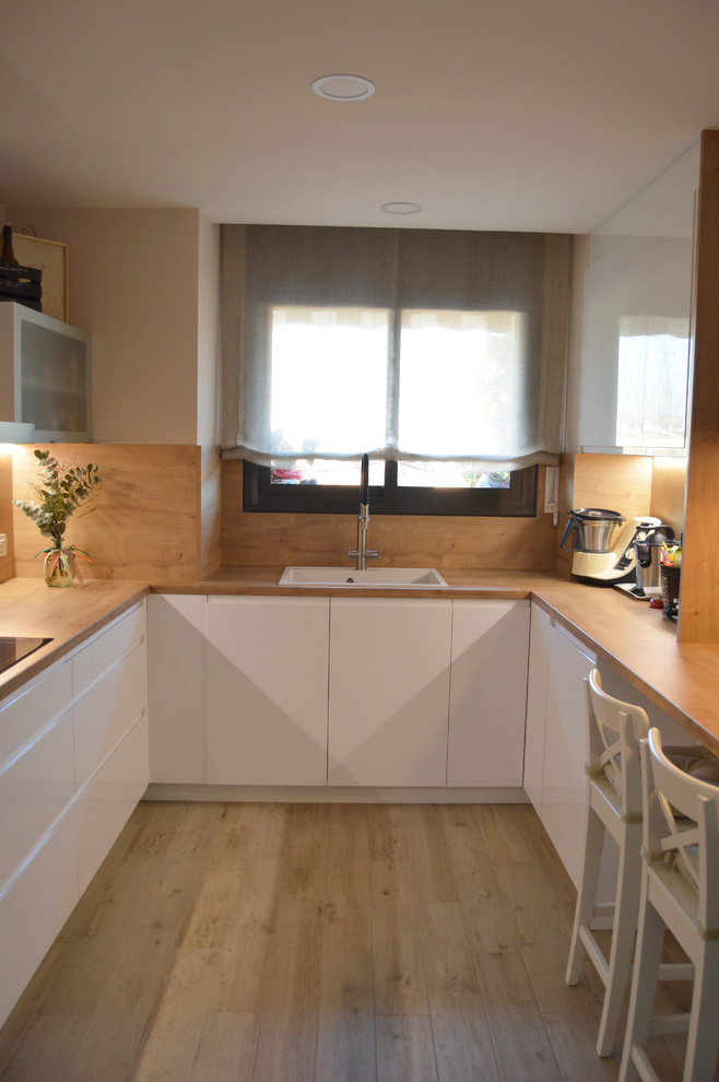 バルセロナにある高級な広い北欧スタイルのおしゃれなキッチン (エプロンフロントシンク、フラットパネル扉のキャビネット、白いキャビネット、ラミネートカウンター、茶色いキッチンパネル、木材のキッチンパネル、シルバーの調理設備、セラミックタイルの床、茶色い床、茶色いキッチンカウンター) の写真