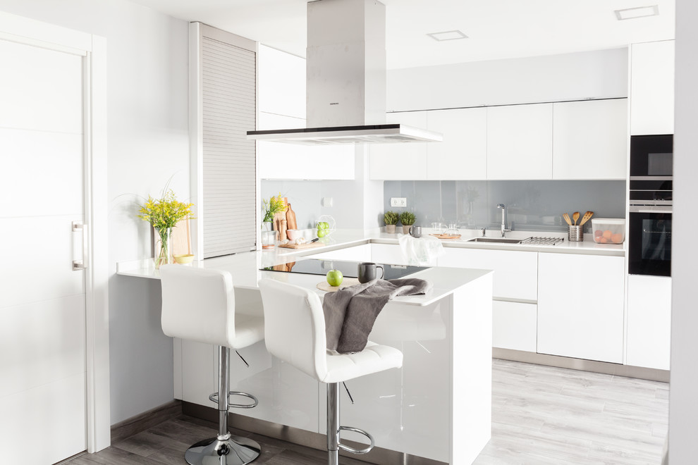 Exempel på ett mellanstort modernt vit vitt u-kök, med en undermonterad diskho, släta luckor, vita skåp, laminatbänkskiva, grått stänkskydd, rostfria vitvaror, laminatgolv, en halv köksö, grått golv och glaspanel som stänkskydd