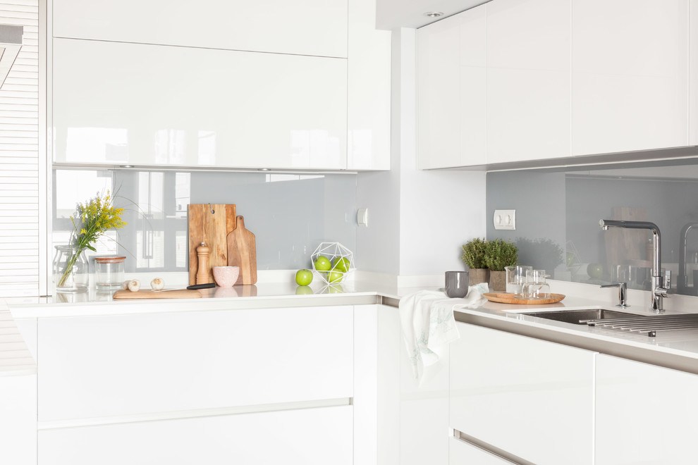 Idéer för mellanstora funkis vitt kök, med en undermonterad diskho, släta luckor, vita skåp, laminatbänkskiva, grått stänkskydd, fönster som stänkskydd, rostfria vitvaror, laminatgolv, en halv köksö och grått golv