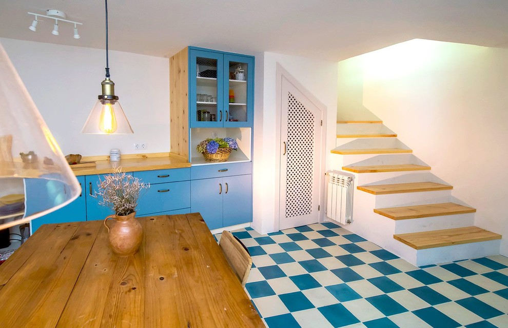 他の地域にあるお手頃価格の中くらいなカントリー風のおしゃれなキッチン (ダブルシンク、ガラス扉のキャビネット、青いキャビネット、木材カウンター、白いキッチンパネル、セラミックタイルのキッチンパネル、黒い調理設備、セラミックタイルの床、アイランドなし、青い床) の写真