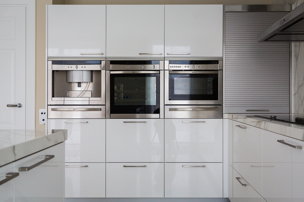 Mittelgroße Wohnküche in L-Form mit flächenbündigen Schrankfronten, weißen Schränken, Quarzwerkstein-Arbeitsplatte, Küchenrückwand in Weiß, Küchengeräten aus Edelstahl, Kücheninsel und weißer Arbeitsplatte in Madrid