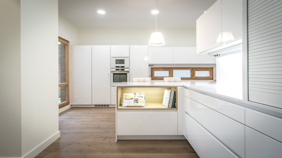 Large modern u-shaped kitchen/diner in Other with a submerged sink, flat-panel cabinets, white cabinets, stainless steel appliances, medium hardwood flooring, a breakfast bar and white worktops.