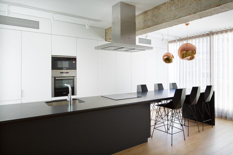 Immagine di una cucina moderna con lavello sottopiano, ante lisce, ante bianche, top in granito, top nero, elettrodomestici da incasso, parquet chiaro e pavimento beige