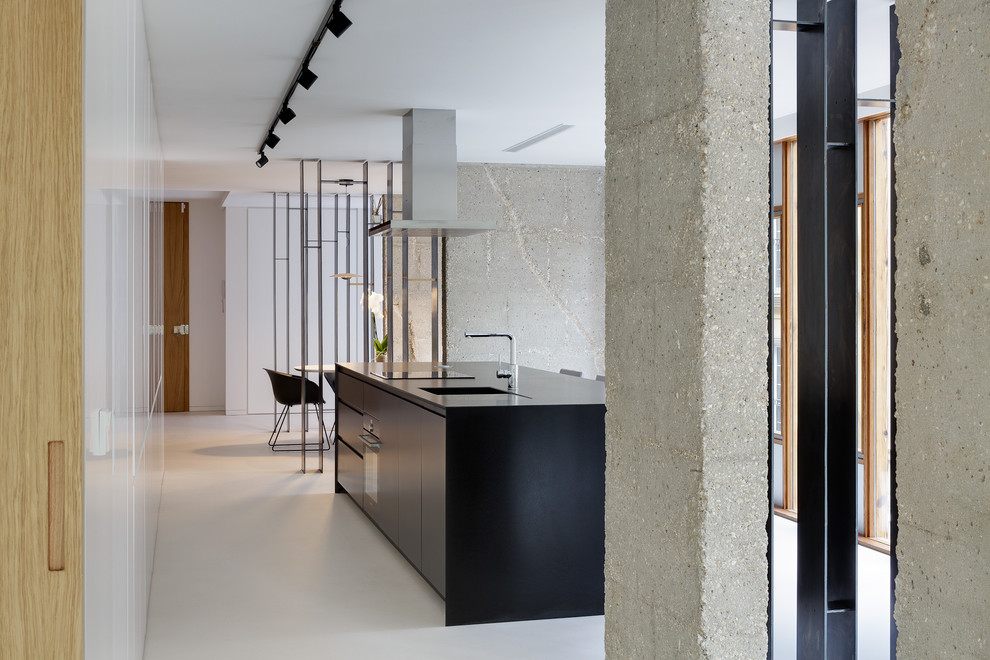 Esempio di una cucina minimalista con lavello sottopiano, ante lisce, ante nere, top in granito, elettrodomestici neri, pavimento in cemento, pavimento bianco e top nero