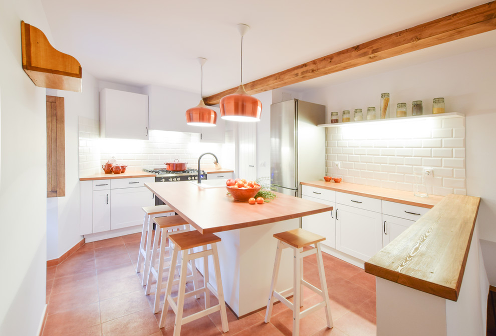 Bild på ett mellanstort medelhavsstil kök, med luckor med upphöjd panel, vita skåp, träbänkskiva, vitt stänkskydd, stänkskydd i tunnelbanekakel, rostfria vitvaror, en köksö och rött golv