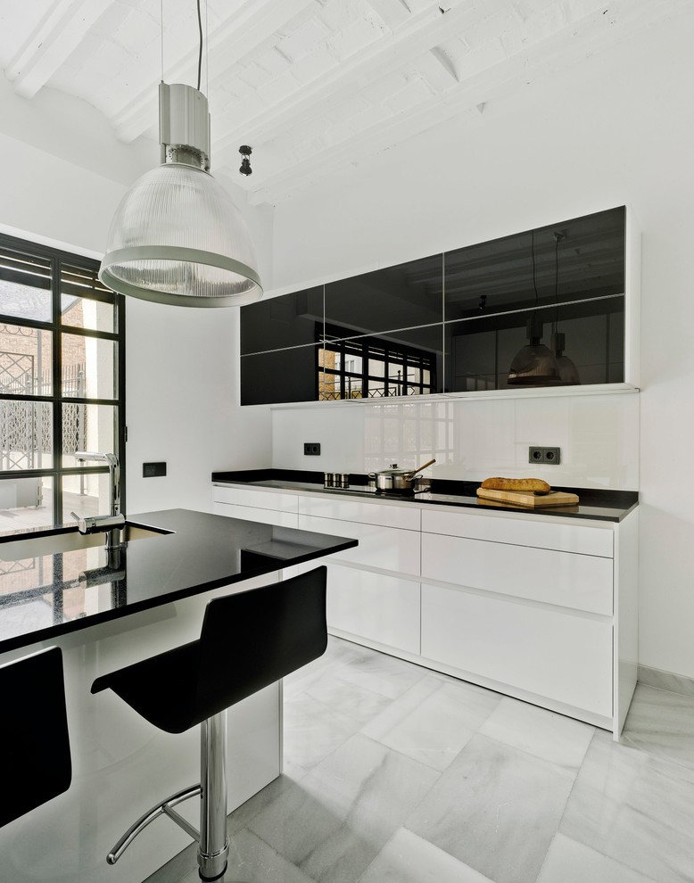 Inspiration for a contemporary kitchen in Madrid with a submerged sink, flat-panel cabinets, white cabinets, granite worktops, white splashback, black appliances, an island, white floors and marble flooring.
