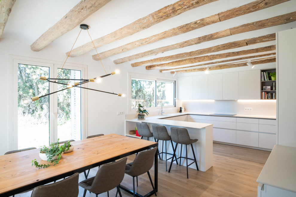 Moderne Küche in U-Form mit flächenbündigen Schrankfronten, weißen Schränken, hellem Holzboden, Halbinsel, beigem Boden und freigelegten Dachbalken in Sonstige