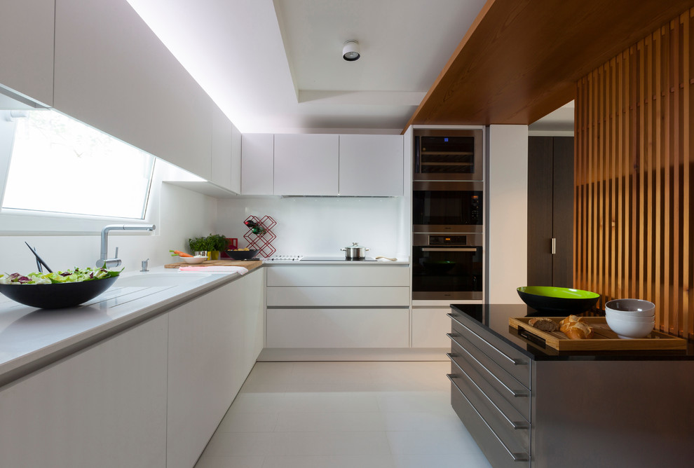 Photo of a medium sized contemporary l-shaped open plan kitchen in Malaga with flat-panel cabinets, white cabinets, white splashback, stainless steel appliances and an island.