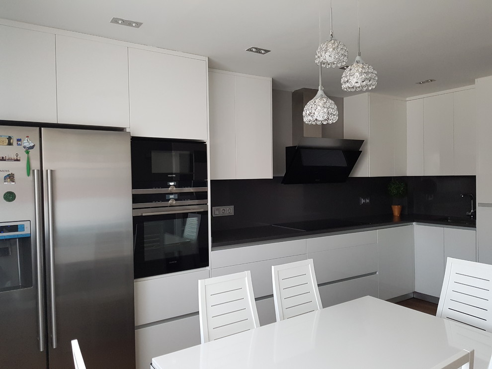 Example of a small minimalist l-shaped dark wood floor and brown floor eat-in kitchen design in Madrid with an undermount sink, flat-panel cabinets, white cabinets, zinc countertops, white backsplash, travertine backsplash, stainless steel appliances, no island and gray countertops