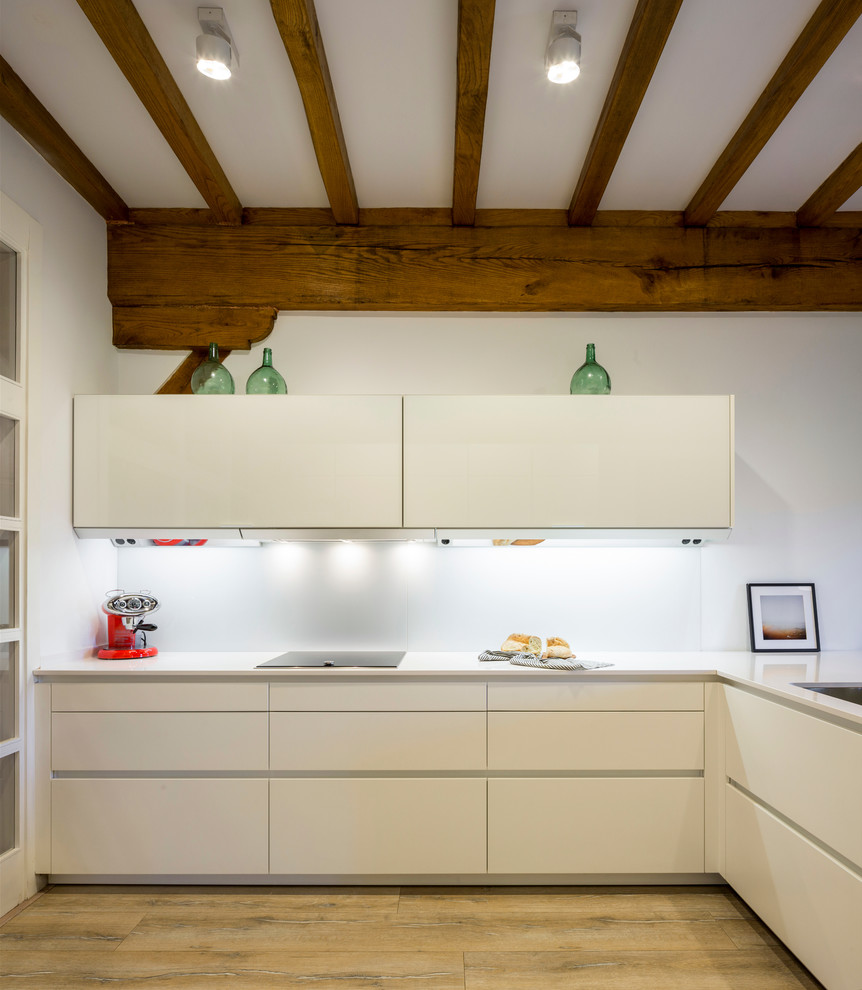 Bild på ett funkis vit vitt l-kök, med släta luckor, vita skåp, vitt stänkskydd och mellanmörkt trägolv