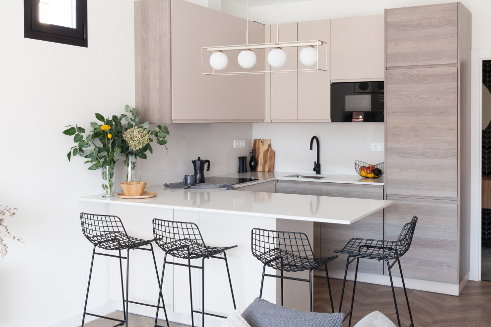 Contemporary u-shaped open plan kitchen in Madrid with a submerged sink, flat-panel cabinets, light wood cabinets, white splashback, integrated appliances, medium hardwood flooring, a breakfast bar, brown floors and white worktops.