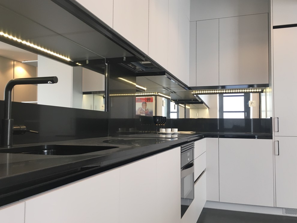 Large modern l-shaped open plan kitchen in Madrid with a submerged sink, flat-panel cabinets, grey cabinets, engineered stone countertops, mirror splashback, black appliances, dark hardwood flooring, no island and black floors.
