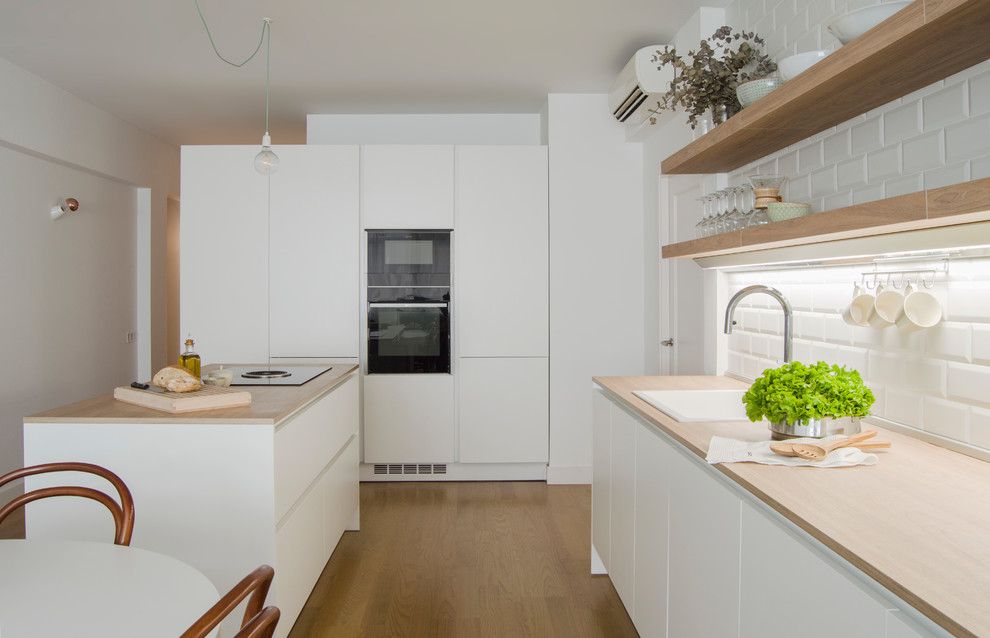 Foto på ett mellanstort funkis brun linjärt kök med öppen planlösning, med en undermonterad diskho, släta luckor, vita skåp, träbänkskiva, rostfria vitvaror, mellanmörkt trägolv, en köksö och brunt golv