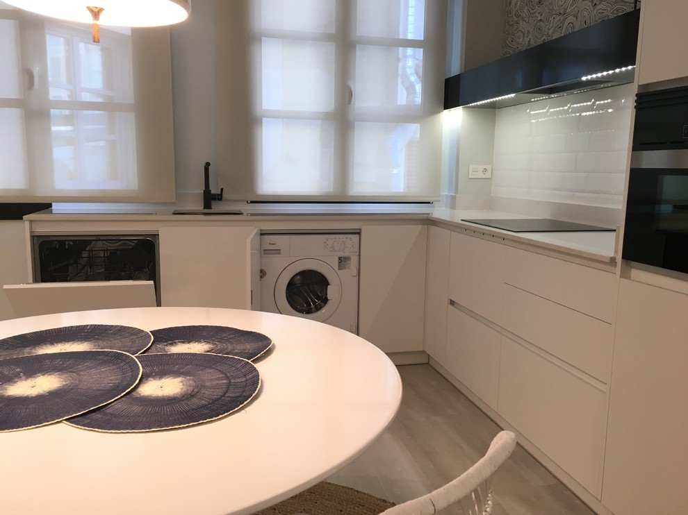 Example of a mid-sized minimalist l-shaped light wood floor open concept kitchen design in Madrid with an undermount sink, flat-panel cabinets, white cabinets, quartz countertops, black backsplash, subway tile backsplash and black appliances