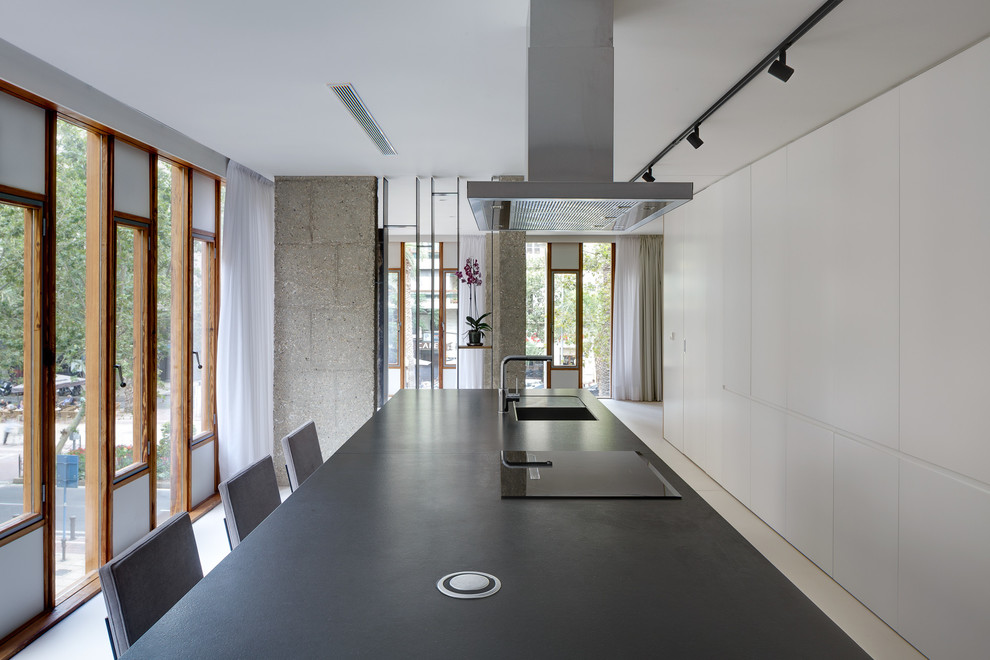 Photo of a modern single-wall open plan kitchen in Alicante-Costa Blanca with a submerged sink, flat-panel cabinets, black cabinets, granite worktops, black appliances, concrete flooring, an island, white floors and black worktops.