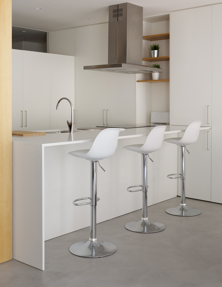 Inredning av ett modernt litet vit vitt kök, med en undermonterad diskho, släta luckor, vita skåp, bänkskiva i kvarts, betonggolv, en köksö och grått golv