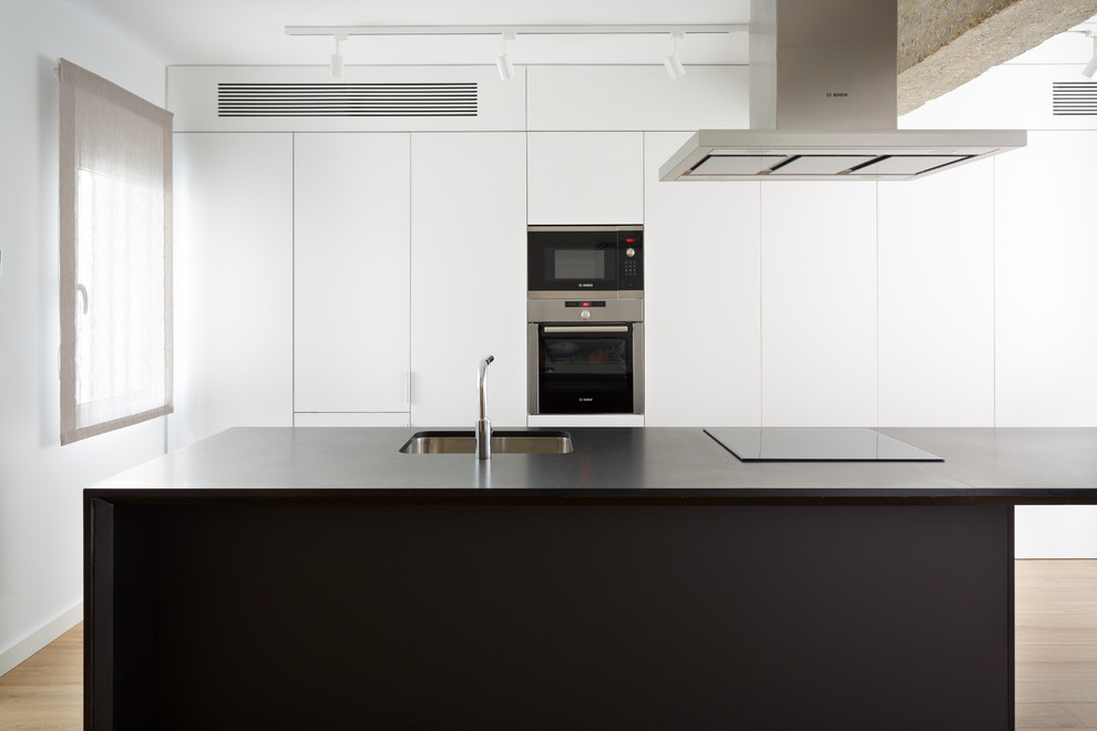 Idéer för funkis linjära svart kök med öppen planlösning, med en undermonterad diskho, släta luckor, vita skåp, granitbänkskiva, rostfria vitvaror, mellanmörkt trägolv och en köksö