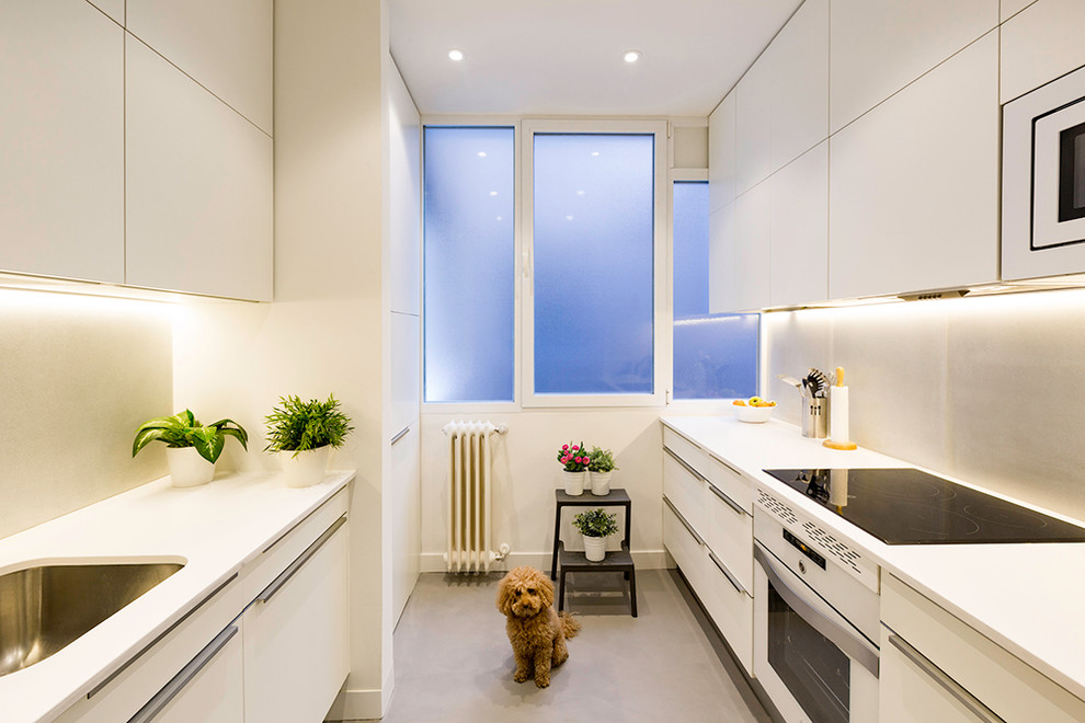 This is an example of a medium sized contemporary galley enclosed kitchen in Madrid with a single-bowl sink, white cabinets, concrete flooring, no island, flat-panel cabinets, white splashback and white appliances.