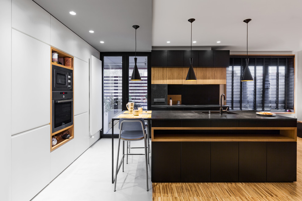 Idéer för stora funkis svart kök, med en undermonterad diskho, släta luckor, svarta skåp, granitbänkskiva, integrerade vitvaror, mellanmörkt trägolv, en köksö och brunt golv
