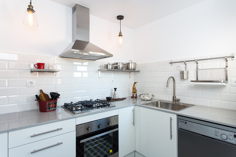 Enclosed kitchen - small industrial l-shaped enclosed kitchen idea in Barcelona with a drop-in sink, flat-panel cabinets, white cabinets, white backsplash, subway tile backsplash, stainless steel appliances, no island and solid surface countertops