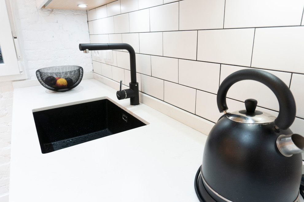 Modern inredning av ett avskilt, mellanstort vit vitt l-kök, med en rustik diskho, vita skåp, kaklad bänkskiva, svart stänkskydd, svarta vitvaror, klinkergolv i keramik, en halv köksö och brunt golv