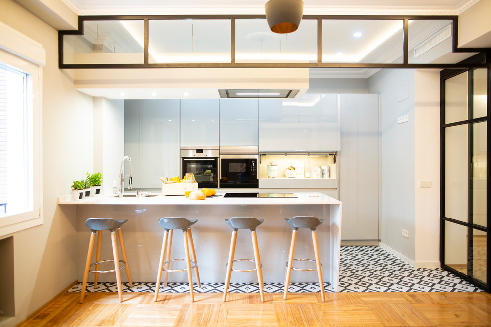 Modern inredning av ett stort vit linjärt vitt kök och matrum, med en dubbel diskho, grå skåp, stänkskydd med metallisk yta, rostfria vitvaror, klinkergolv i keramik, en köksö och flerfärgat golv