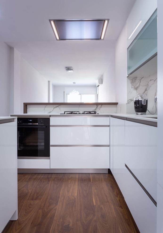 Inspiration for a small contemporary l-shaped dark wood floor and brown floor open concept kitchen remodel in Barcelona with a single-bowl sink, flat-panel cabinets, white cabinets, white backsplash, stainless steel appliances, a peninsula and white countertops