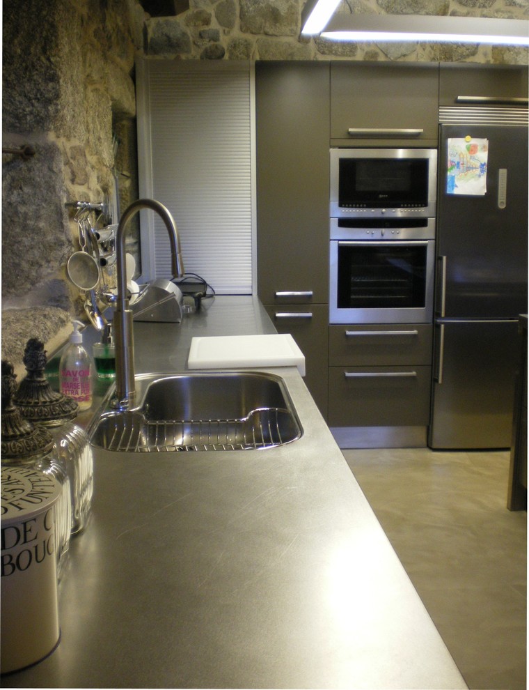 Rustik inredning av ett stort kök, med en nedsänkt diskho, skåp i rostfritt stål, bänkskiva i rostfritt stål, rostfria vitvaror, betonggolv, en köksö och beiget golv