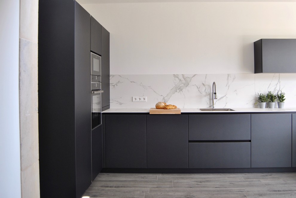 Moderne Küche ohne Insel in L-Form mit flächenbündigen Schrankfronten, schwarzen Schränken, Küchenrückwand in Weiß, weißer Arbeitsplatte, Waschbecken, Elektrogeräten mit Frontblende und grauem Boden in Bilbao