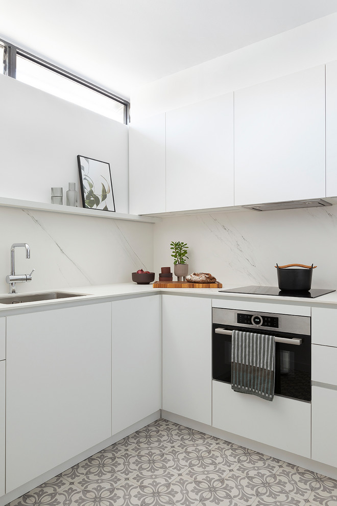 Contemporary l-shaped kitchen in Barcelona with a submerged sink, flat-panel cabinets, white cabinets, white splashback, stone slab splashback, stainless steel appliances, multi-coloured floors and white worktops.