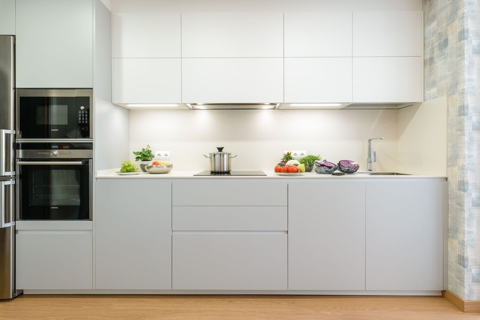 Inspiration for a modern single-wall enclosed kitchen in Malaga with a built-in sink, flat-panel cabinets, grey cabinets, white splashback, stainless steel appliances, medium hardwood flooring and no island.