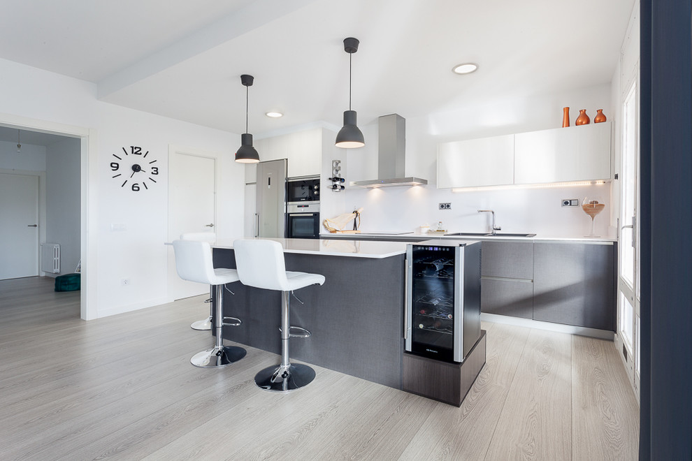 This is an example of a medium sized contemporary grey and white single-wall open plan kitchen in Other with flat-panel cabinets, grey cabinets, an island, white splashback, stainless steel appliances, a double-bowl sink, light hardwood flooring, engineered stone countertops, metal splashback, grey floors and white worktops.