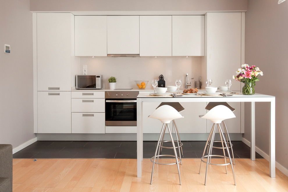 Diseño de cocina lineal contemporánea de tamaño medio con puertas de armario blancas, armarios con paneles lisos, electrodomésticos de acero inoxidable, suelo de madera clara y una isla
