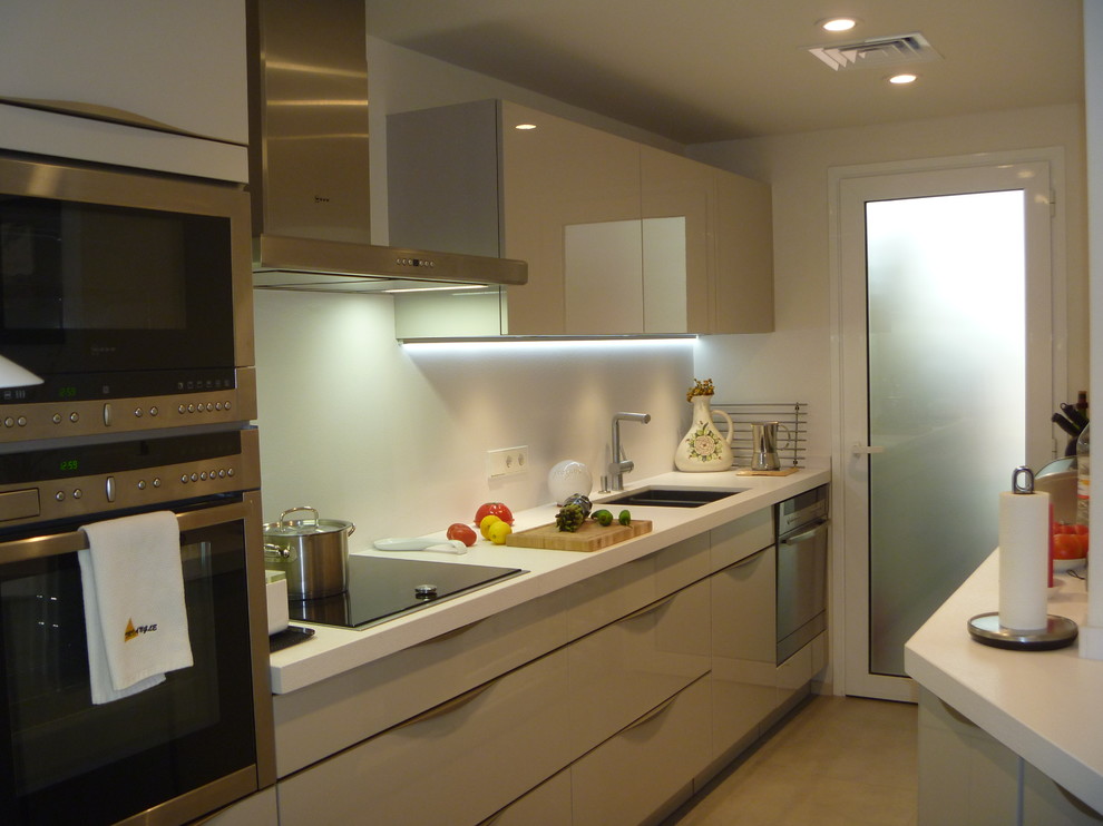 This is an example of a medium sized contemporary galley enclosed kitchen in Barcelona with a single-bowl sink, flat-panel cabinets, white cabinets, white splashback, stainless steel appliances and no island.