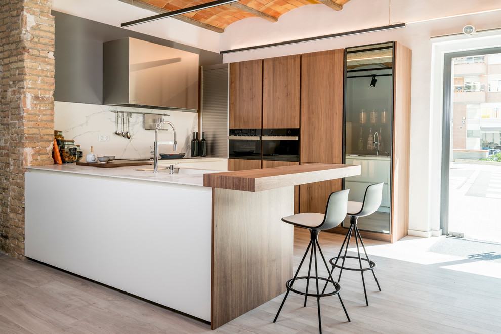 Modern inredning av ett mellanstort kök, med släta luckor, skåp i mellenmörkt trä, marmorbänkskiva, rostfria vitvaror, ljust trägolv och en halv köksö