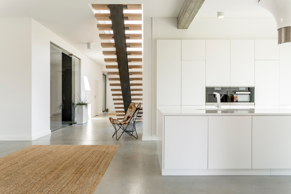 Idéer för stora funkis linjära vitt kök med öppen planlösning, med en undermonterad diskho, släta luckor, vita skåp, bänkskiva i kvarts, vitt stänkskydd, fönster som stänkskydd, integrerade vitvaror, betonggolv, en köksö och grått golv