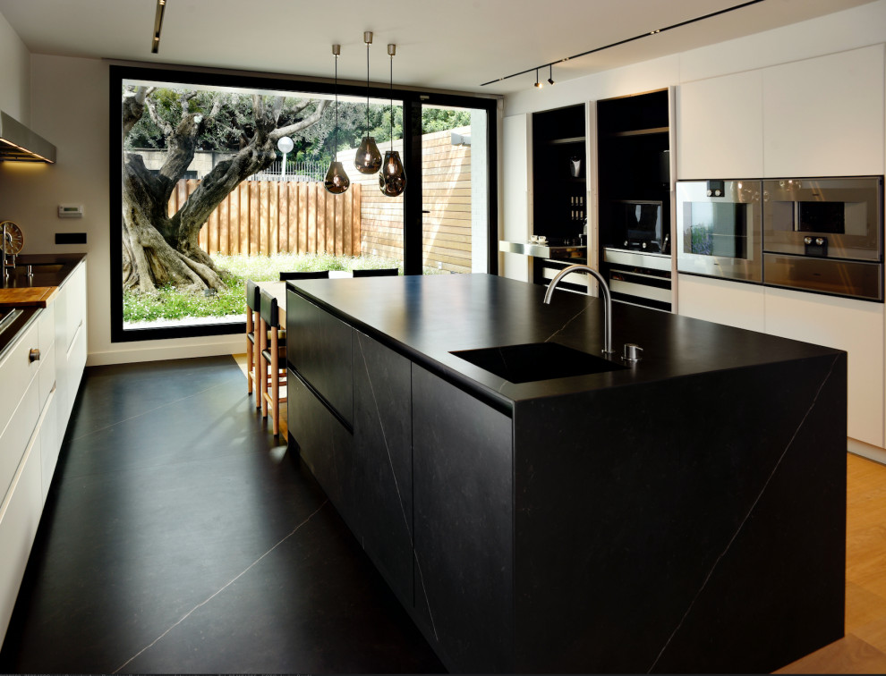 Foto på ett mycket stort funkis svart linjärt kök med öppen planlösning, med en integrerad diskho, släta luckor, vita skåp, bänkskiva i kvarts, svart stänkskydd, rostfria vitvaror, ljust trägolv, en köksö och brunt golv