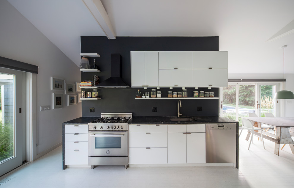 Modern inredning av ett svart linjärt svart kök med öppen planlösning, med en undermonterad diskho, släta luckor, vita skåp, rostfria vitvaror och vitt golv