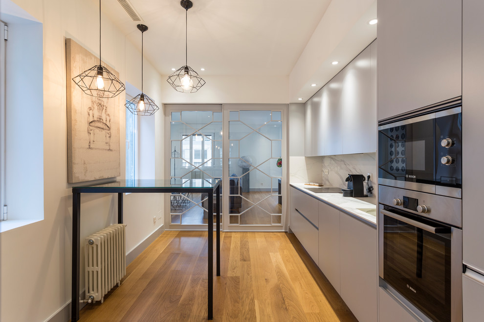 Kitchen - mid-sized contemporary single-wall medium tone wood floor kitchen idea in Madrid with flat-panel cabinets, gray cabinets, marble countertops, white backsplash, marble backsplash, stainless steel appliances and white countertops