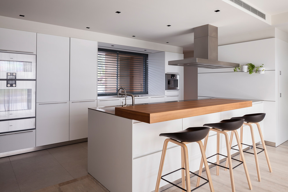 Diseño de cocinas en L contemporánea con armarios con paneles lisos, puertas de armario blancas, electrodomésticos de acero inoxidable, una isla y suelo gris