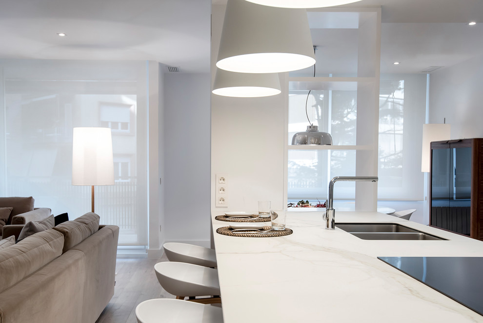 Offene Moderne Küche mit Unterbauwaschbecken, flächenbündigen Schrankfronten, weißen Schränken, Küchenrückwand in Weiß, Küchengeräten aus Edelstahl, hellem Holzboden und Kücheninsel in Barcelona