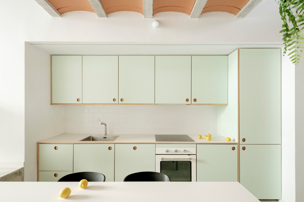 Exempel på ett litet skandinaviskt grön linjärt grönt kök med öppen planlösning, med en nedsänkt diskho, skåp i shakerstil, gröna skåp, laminatbänkskiva, vitt stänkskydd, stänkskydd i keramik, rostfria vitvaror, betonggolv och grått golv