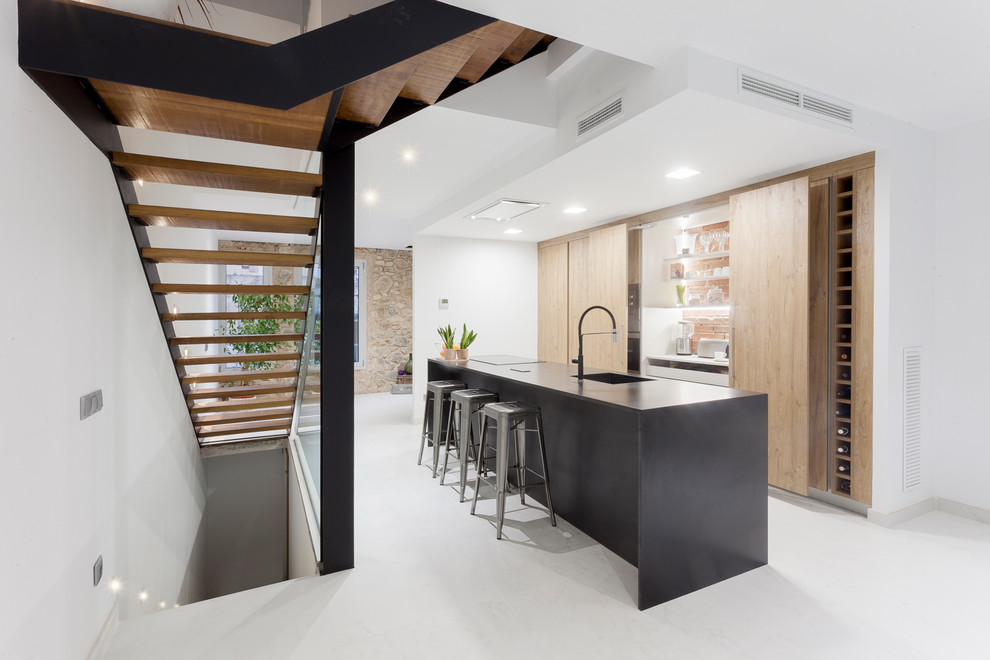Пример оригинального дизайна: прямая кухня в стиле модернизм с плоскими фасадами, островом, черной столешницей, одинарной мойкой, светлыми деревянными фасадами и белым полом
