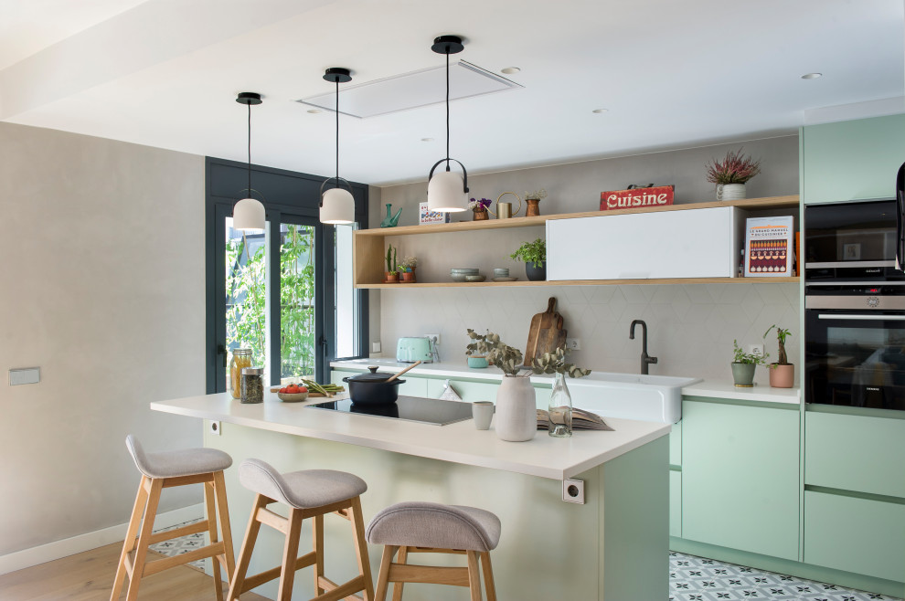 Open concept kitchen - contemporary galley multicolored floor open concept kitchen idea in Barcelona with a farmhouse sink, flat-panel cabinets, green cabinets, gray backsplash, stainless steel appliances, an island and white countertops