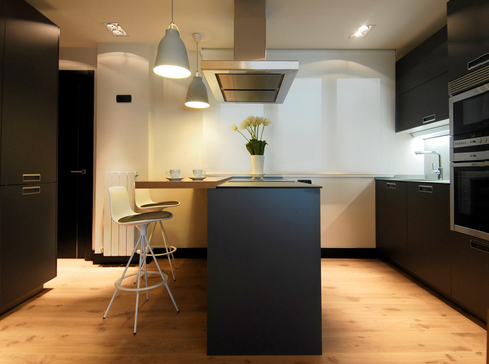 Modern inredning av ett mellanstort linjärt kök med öppen planlösning, med släta luckor, svarta skåp, svart stänkskydd, integrerade vitvaror, ljust trägolv, en köksö och en undermonterad diskho