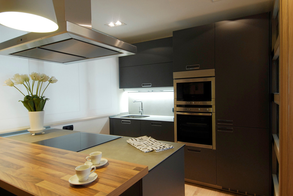 Medium sized contemporary single-wall open plan kitchen in Bilbao with recessed-panel cabinets, black cabinets, medium hardwood flooring, a submerged sink, a breakfast bar, stainless steel appliances and grey splashback.